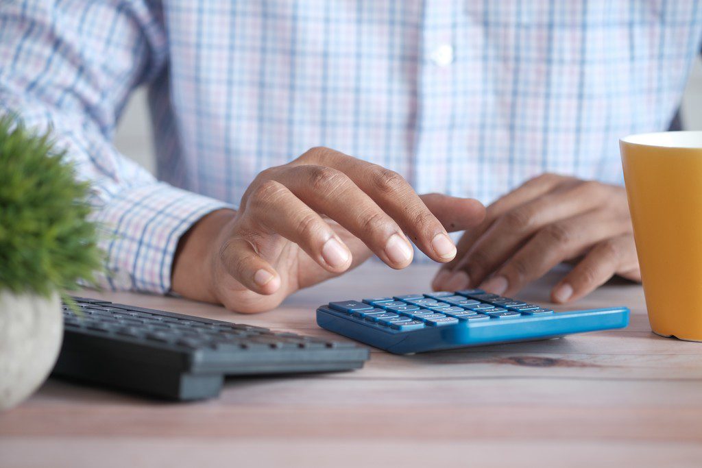 Pessoa usando calculadora, que está ao lado de um teclado de computador, simbolizando DEFIS Simples Nacional